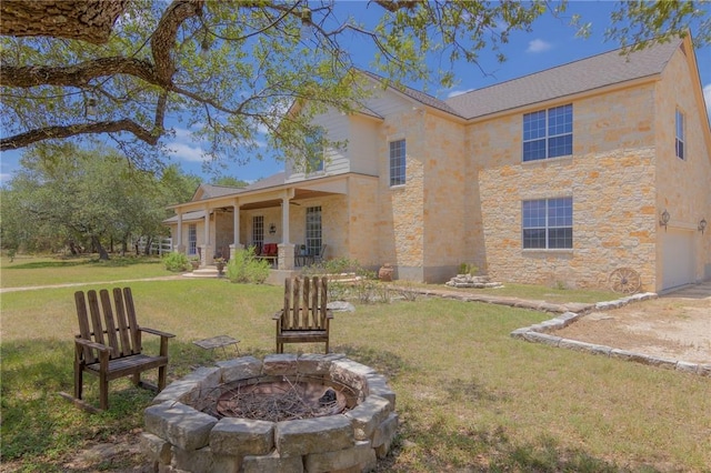 rear view of house with an outdoor fire pit, stone siding, a garage, a porch, and a lawn