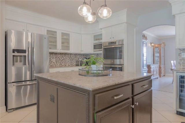 kitchen featuring arched walkways, appliances with stainless steel finishes, light tile patterned floors, and a kitchen island