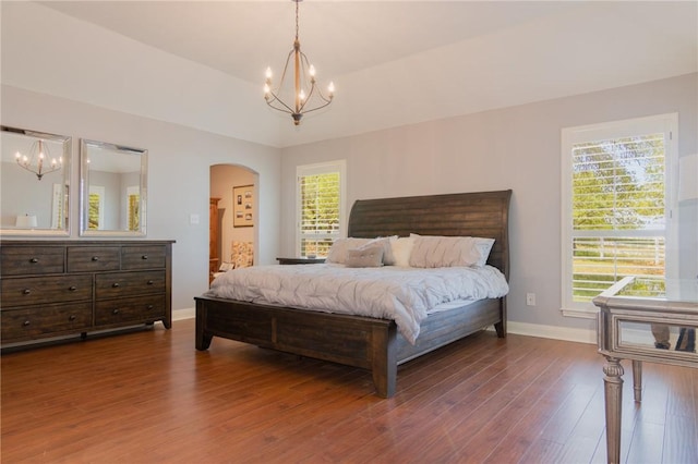 bedroom with baseboards, arched walkways, dark wood-style flooring, and a notable chandelier