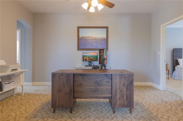 office area with baseboards, arched walkways, a ceiling fan, and light carpet