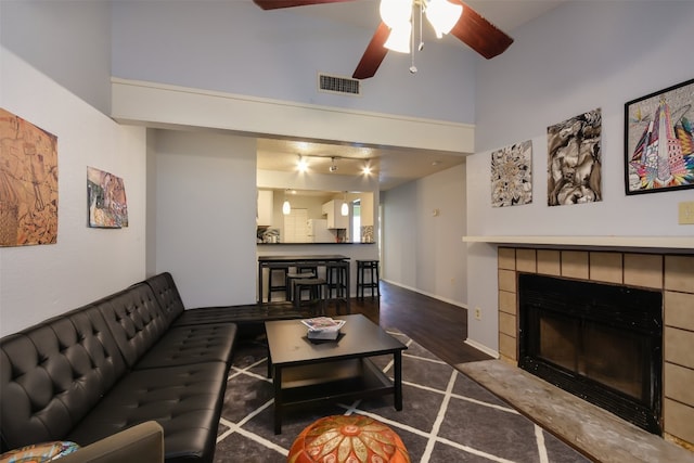 living area with ceiling fan, visible vents, a fireplace, wood finished floors, and a high ceiling