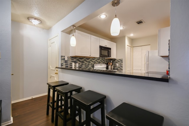 kitchen featuring decorative backsplash, visible vents, black microwave, dark countertops, and freestanding refrigerator