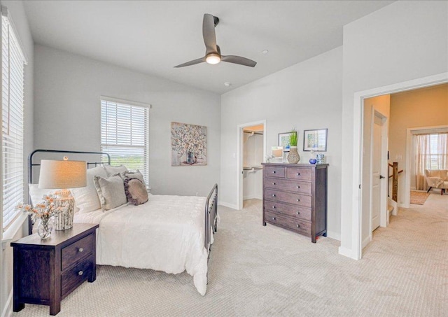 bedroom featuring light carpet, a walk in closet, a ceiling fan, baseboards, and a closet
