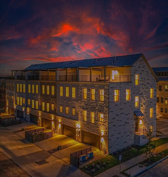 back of house at dusk with a garage, a standing seam roof, metal roof, and a balcony