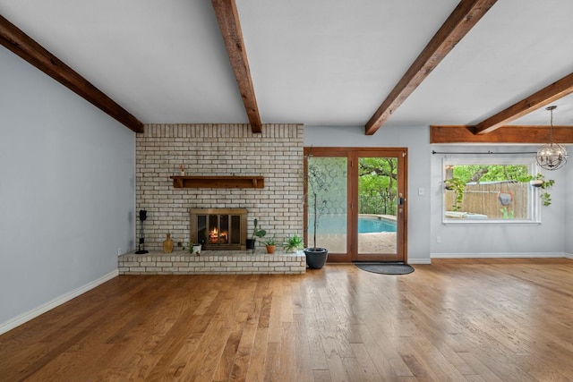 unfurnished living room with a brick fireplace, baseboards, wood finished floors, and beamed ceiling