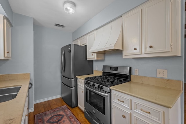 kitchen featuring visible vents, wood finished floors, light countertops, ventilation hood, and appliances with stainless steel finishes