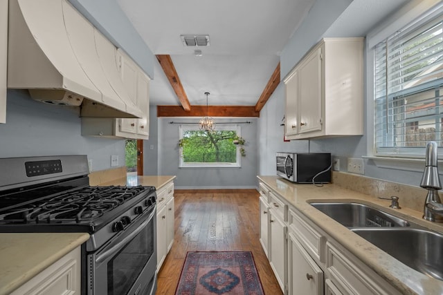 kitchen featuring appliances with stainless steel finishes, a sink, under cabinet range hood, beamed ceiling, and visible vents