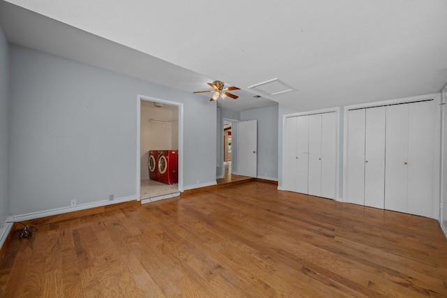 unfurnished bedroom featuring multiple closets, baseboards, attic access, and wood finished floors
