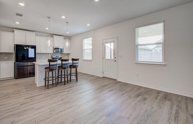 kitchen featuring a kitchen breakfast bar, visible vents, tasteful backsplash, light wood-style floors, and stainless steel appliances