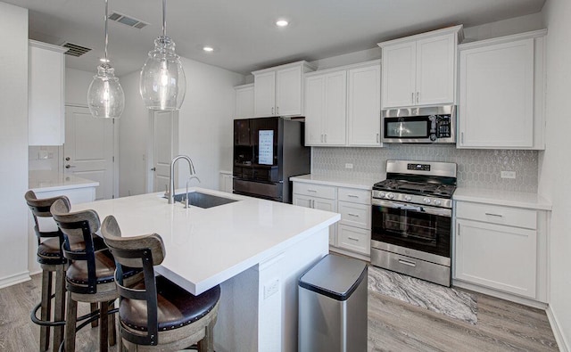 kitchen with visible vents, light wood-style floors, an island with sink, a sink, and stainless steel appliances