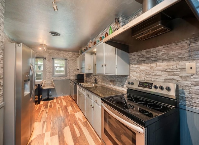 1207 Flag St, Llano, TX 78643 - kitchen featuring a sink, light wood-style floors, stainless steel appliances, white cabinetry, and under cabinet range hood