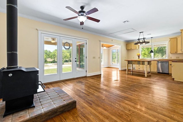 living area with visible vents, a wood stove, ornamental molding, wood finished floors, and a ceiling fan