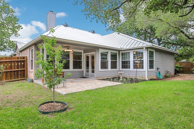 rear view of property with ceiling fan, a fenced backyard, a chimney, a yard, and metal roof
