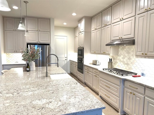 kitchen with tasteful backsplash, a sink, light stone counters, under cabinet range hood, and stainless steel appliances