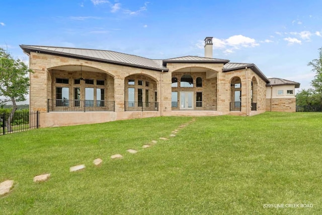 rear view of property featuring a standing seam roof, a chimney, a lawn, and french doors