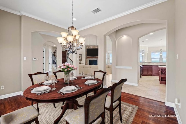 dining space with visible vents, arched walkways, light wood finished floors, a chandelier, and ornamental molding