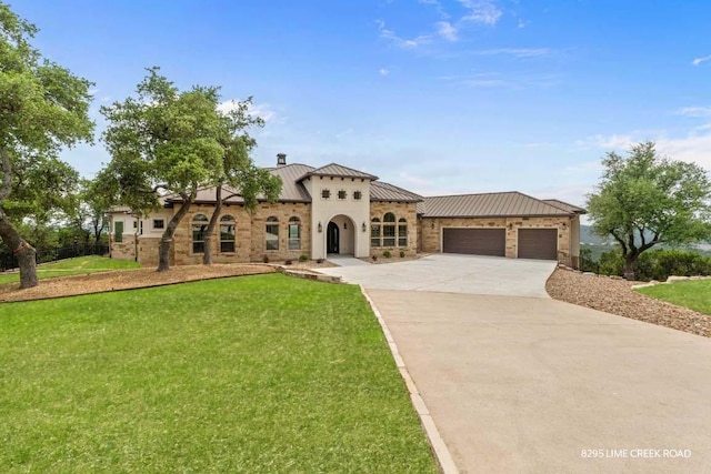 mediterranean / spanish-style house featuring a front lawn, stone siding, a standing seam roof, an attached garage, and driveway