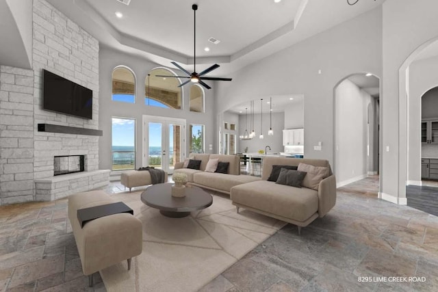 living area with arched walkways, a stone fireplace, french doors, stone tile floors, and baseboards