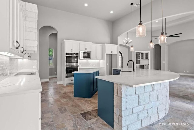 kitchen with arched walkways, appliances with stainless steel finishes, a spacious island, a sink, and stone tile floors