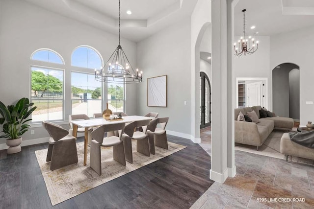 dining room with an inviting chandelier, arched walkways, baseboards, a towering ceiling, and a tray ceiling