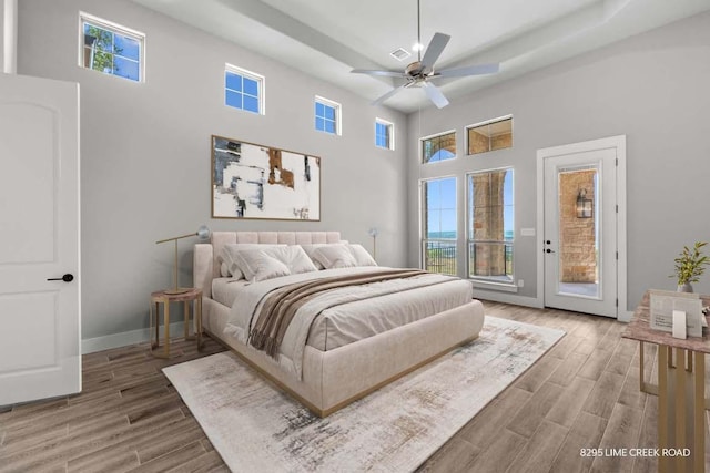 bedroom with a raised ceiling, a high ceiling, wood finished floors, and access to exterior