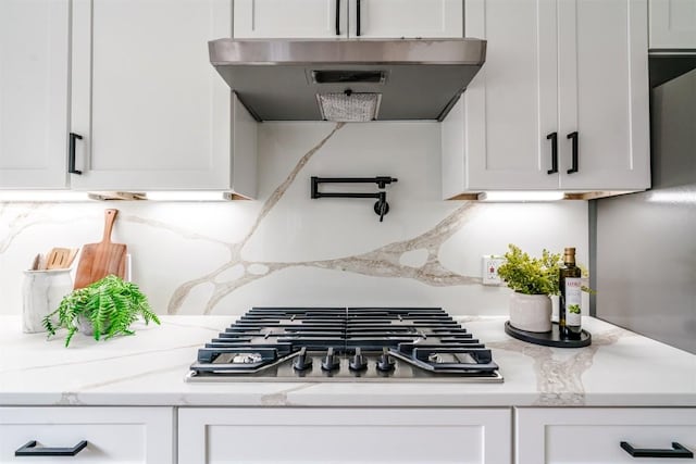 kitchen with under cabinet range hood, stainless steel gas stovetop, white cabinets, decorative backsplash, and light stone counters