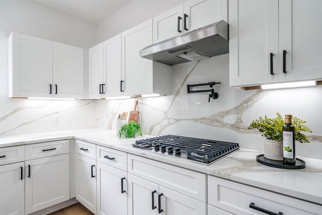 kitchen featuring under cabinet range hood, white cabinets, stainless steel gas cooktop, tasteful backsplash, and light stone countertops