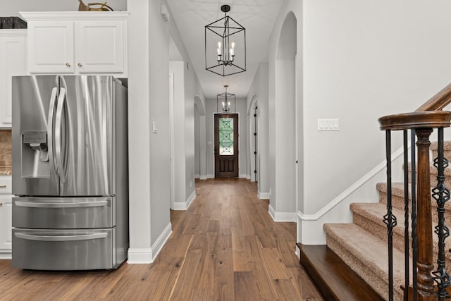 foyer with arched walkways, baseboards, an inviting chandelier, and wood finished floors