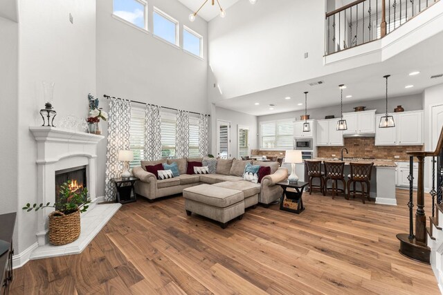 living room featuring a lit fireplace, light wood finished floors, and a towering ceiling