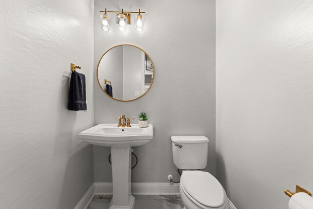 half bath with baseboards, toilet, and marble finish floor