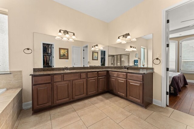 bathroom with tiled bath, a notable chandelier, a sink, tile patterned flooring, and double vanity