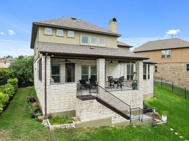 back of house featuring fence, stone siding, a lawn, a ceiling fan, and a patio