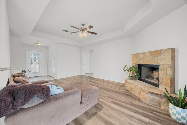 living area featuring visible vents, a ceiling fan, wood finished floors, and a tray ceiling