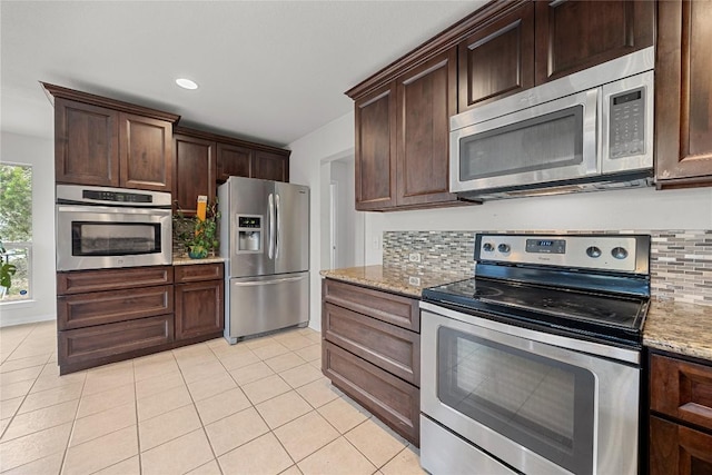 kitchen featuring dark brown cabinets, light stone countertops, light tile patterned floors, appliances with stainless steel finishes, and backsplash