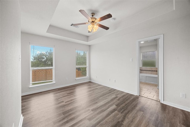unfurnished bedroom featuring connected bathroom, dark wood finished floors, baseboards, a tray ceiling, and visible vents
