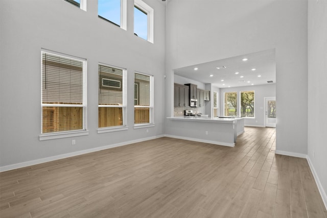 2705 Sage Ranch Dr Unit 25, Leander, TX 78641 - unfurnished living room featuring light wood-style flooring, baseboards, a towering ceiling, and recessed lighting