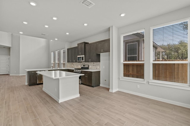 2705 Sage Ranch Dr Unit 25, Leander, TX 78641 - kitchen featuring appliances with stainless steel finishes, a kitchen island, light countertops, light wood-style flooring, and backsplash