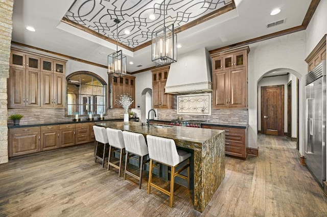 kitchen featuring a sink, a raised ceiling, arched walkways, stainless steel appliances, and custom exhaust hood