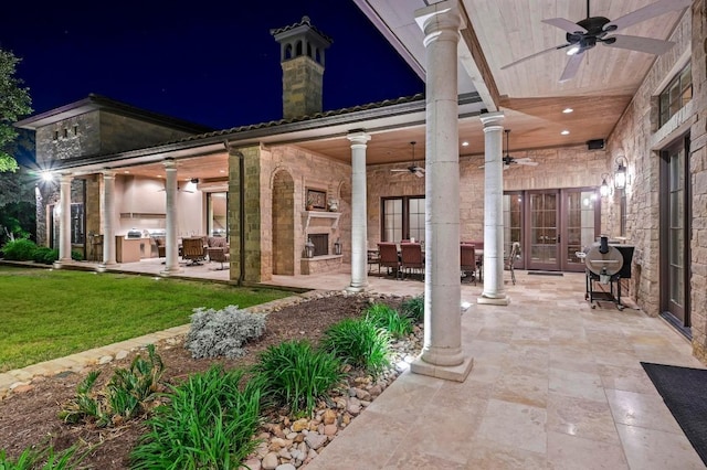 patio at twilight featuring an outdoor stone fireplace, french doors, a ceiling fan, a yard, and outdoor dining space