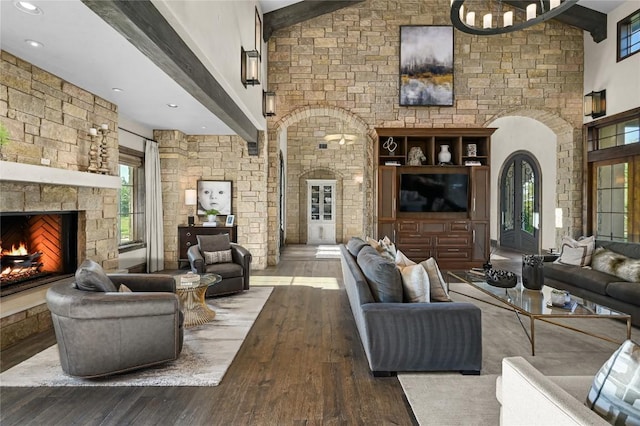 living room with arched walkways, a stone fireplace, beam ceiling, and hardwood / wood-style flooring