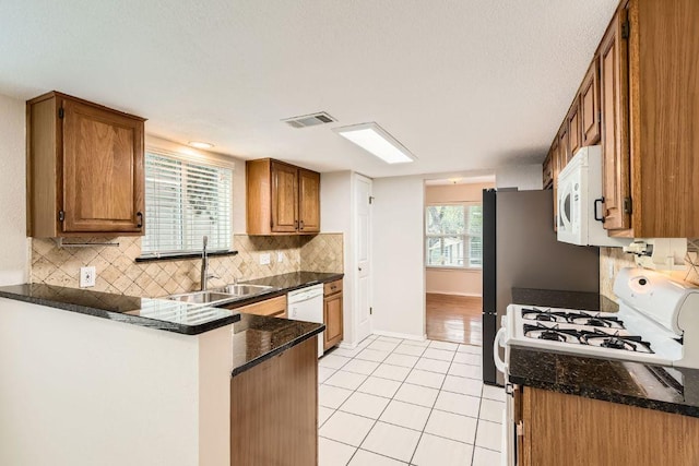 4318 Clarno Dr, Austin, TX 78749 - kitchen featuring white appliances, light tile patterned floors, brown cabinetry, decorative backsplash, and a peninsula