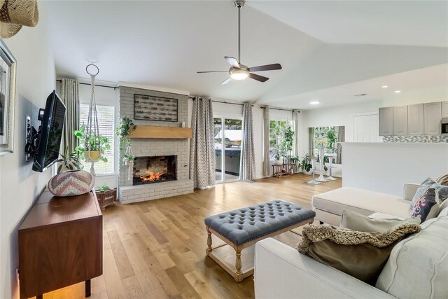 living room featuring a ceiling fan, vaulted ceiling, a brick fireplace, light wood-style floors, and recessed lighting