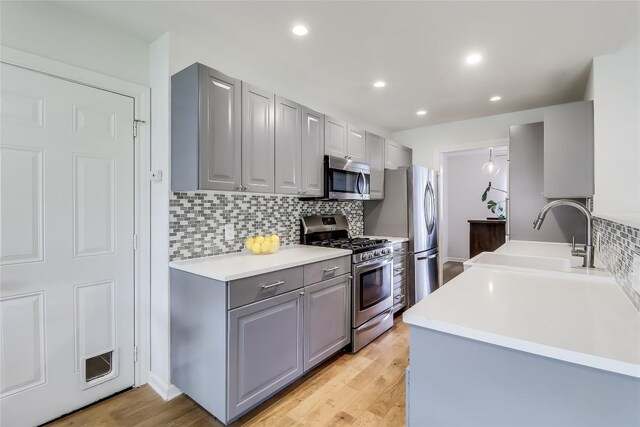 kitchen with a sink, light wood-style flooring, stainless steel appliances, backsplash, and gray cabinetry