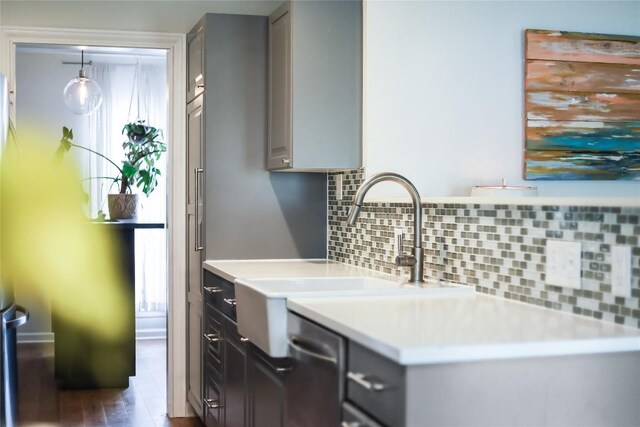 kitchen with light countertops, a sink, gray cabinets, and tasteful backsplash