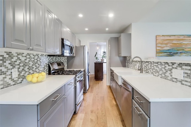 kitchen with a sink, gray cabinets, stainless steel appliances, and light wood finished floors