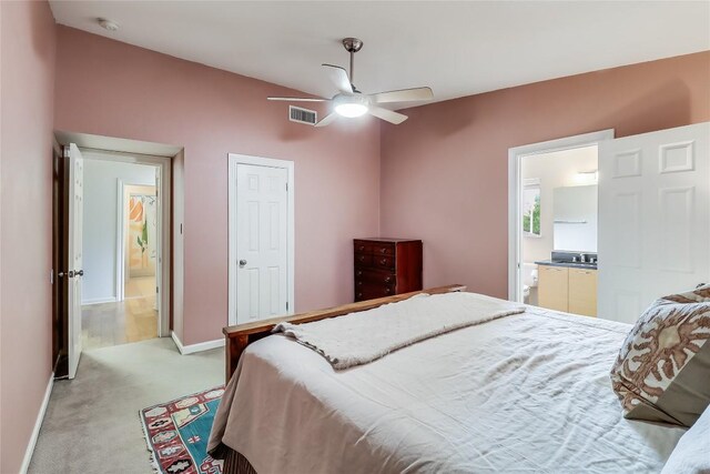 bedroom featuring ceiling fan, light colored carpet, visible vents, baseboards, and ensuite bathroom