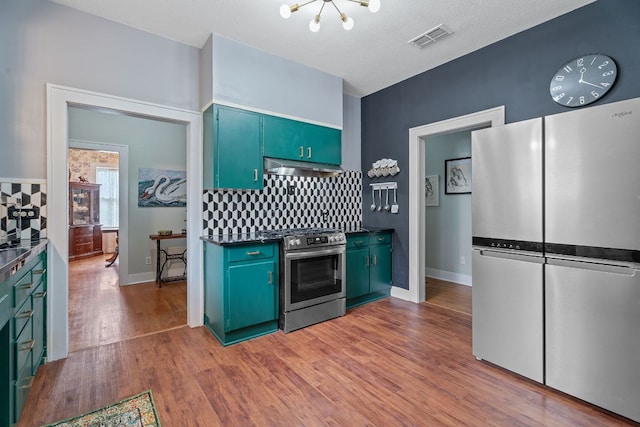 kitchen with dark countertops, appliances with stainless steel finishes, a chandelier, decorative backsplash, and visible vents