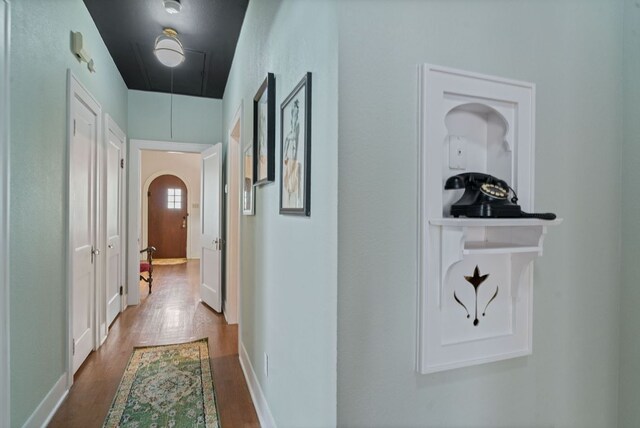 hallway featuring arched walkways, baseboards, attic access, and wood finished floors