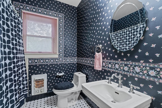 bathroom with heating unit, wallpapered walls, toilet, and a sink