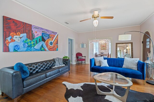 living area featuring visible vents, a ceiling fan, crown molding, and wood finished floors